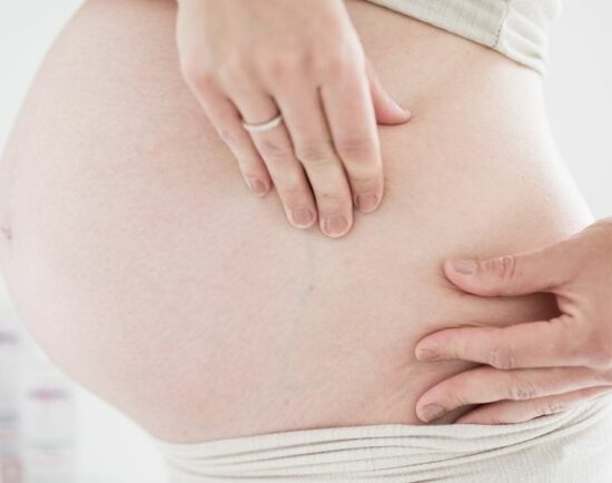 Frau streichelt und massiert Bauch gegen Dehnungsstreifen
