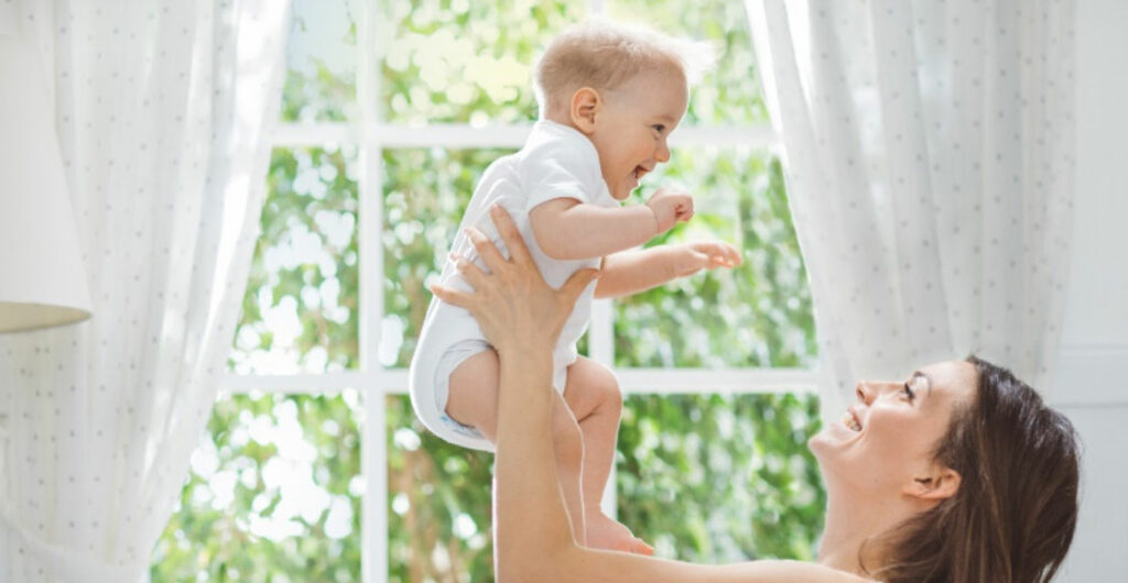 Mama, die ihr Baby in die Luft hebt