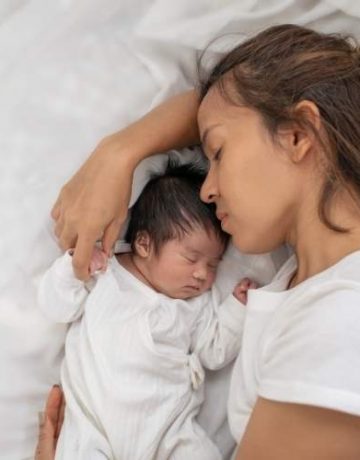 Frau liegt mit ihrem Baby auf einem Bett
