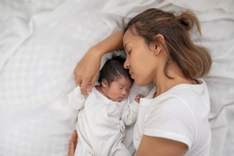 Frau liegt mit ihrem Baby auf einem Bett